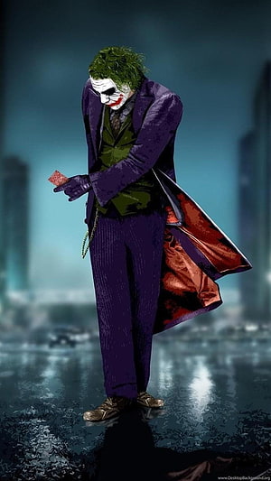 The Joker in a purple suit holding a playing card in a rainy cityscape HD phone wallpaper
