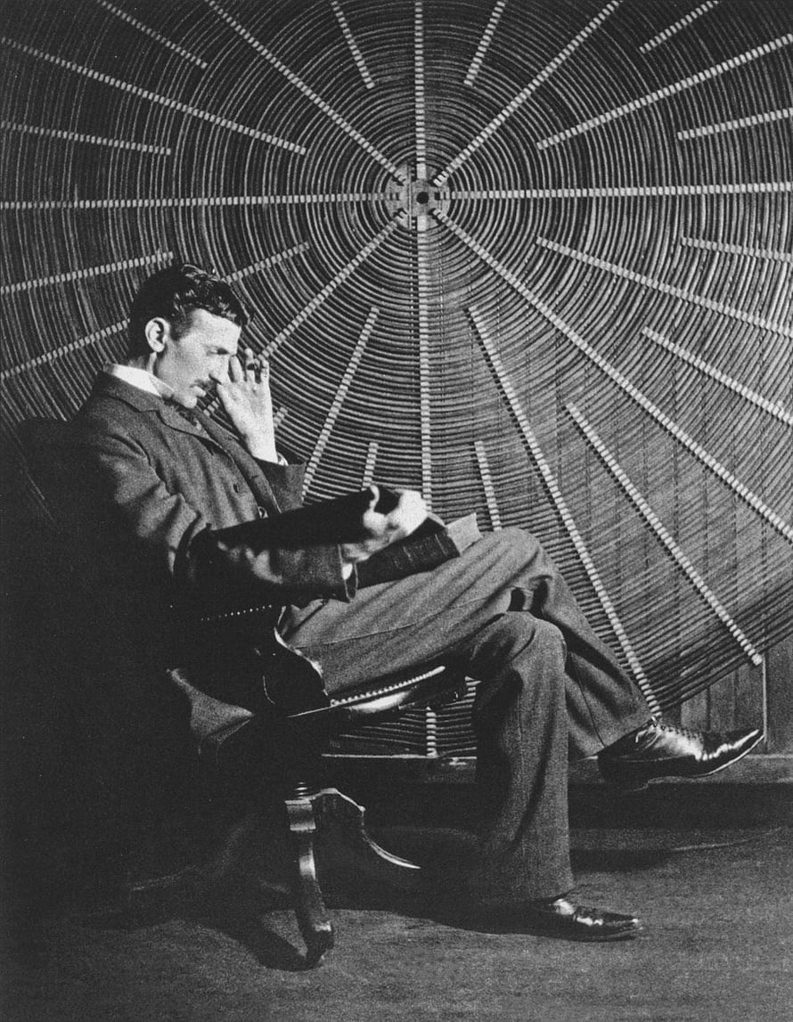 Nikola Tesla seated in front of a large radial coil apparatus in a vintage black and white photograph HD phone wallpaper