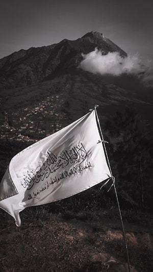 White Islamic Flag with Arabic Calligraphy Waving Against a Dark Mountain Landscape HD phone wallpaper