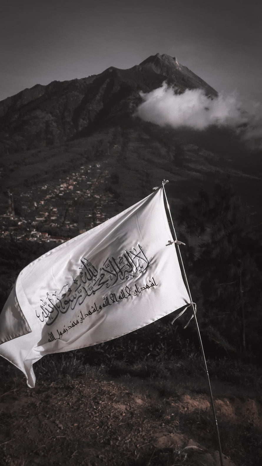 White Islamic Flag with Arabic Calligraphy Waving Against a Dark Mountain Landscape HD phone wallpaper