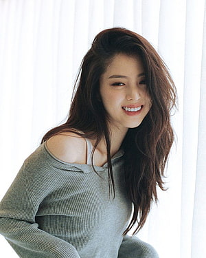 Han So Hee smiling portrait in a grey off-shoulder knit sweater with soft natural window light HD phone wallpaper