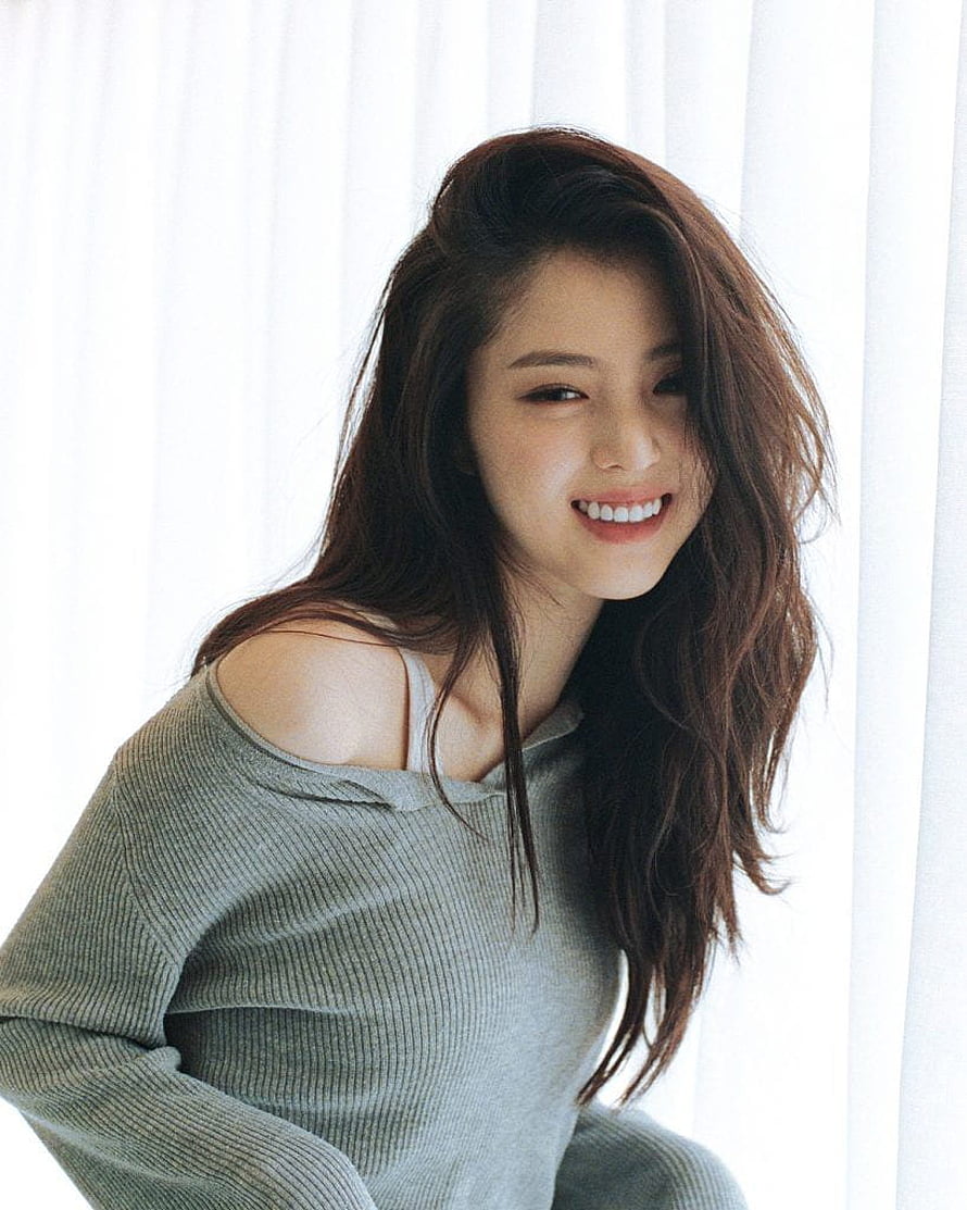 Han So Hee smiling portrait in a grey off-shoulder knit sweater with soft natural window light HD phone wallpaper