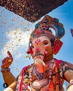 Vibrant Ganesha Idol With Flower Petals Falling Against Blue Sky HD phone wallpaper