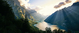 Sunbeams Breaking Through Clouds Over a Serene Mountain Lake and Forested Valley HD wallpaper