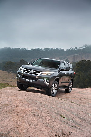 Dark Grey Toyota Fortuner SUV Parked on Rocky Outcrop with Forest Background HD phone wallpaper