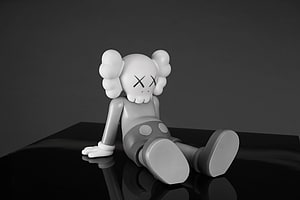 KAWS Companion Figure in Monochrome Sitting on a Reflective Black Surface HD wallpaper