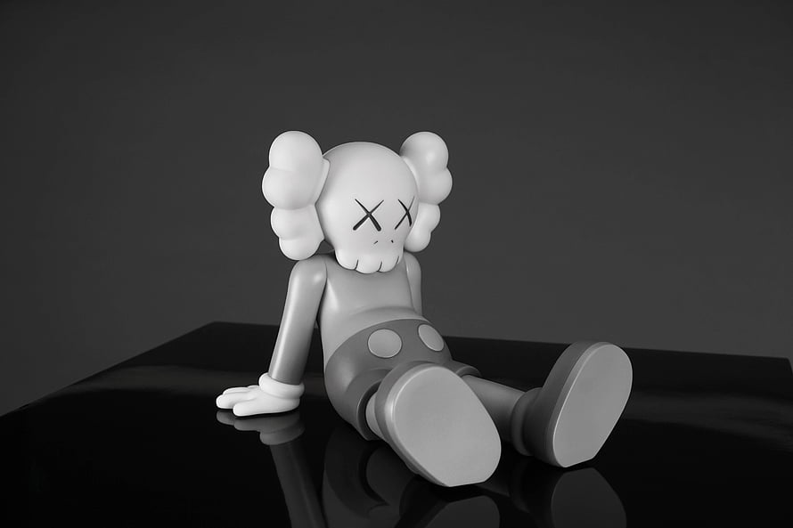 KAWS Companion Figure in Monochrome Sitting on a Reflective Black Surface HD wallpaper