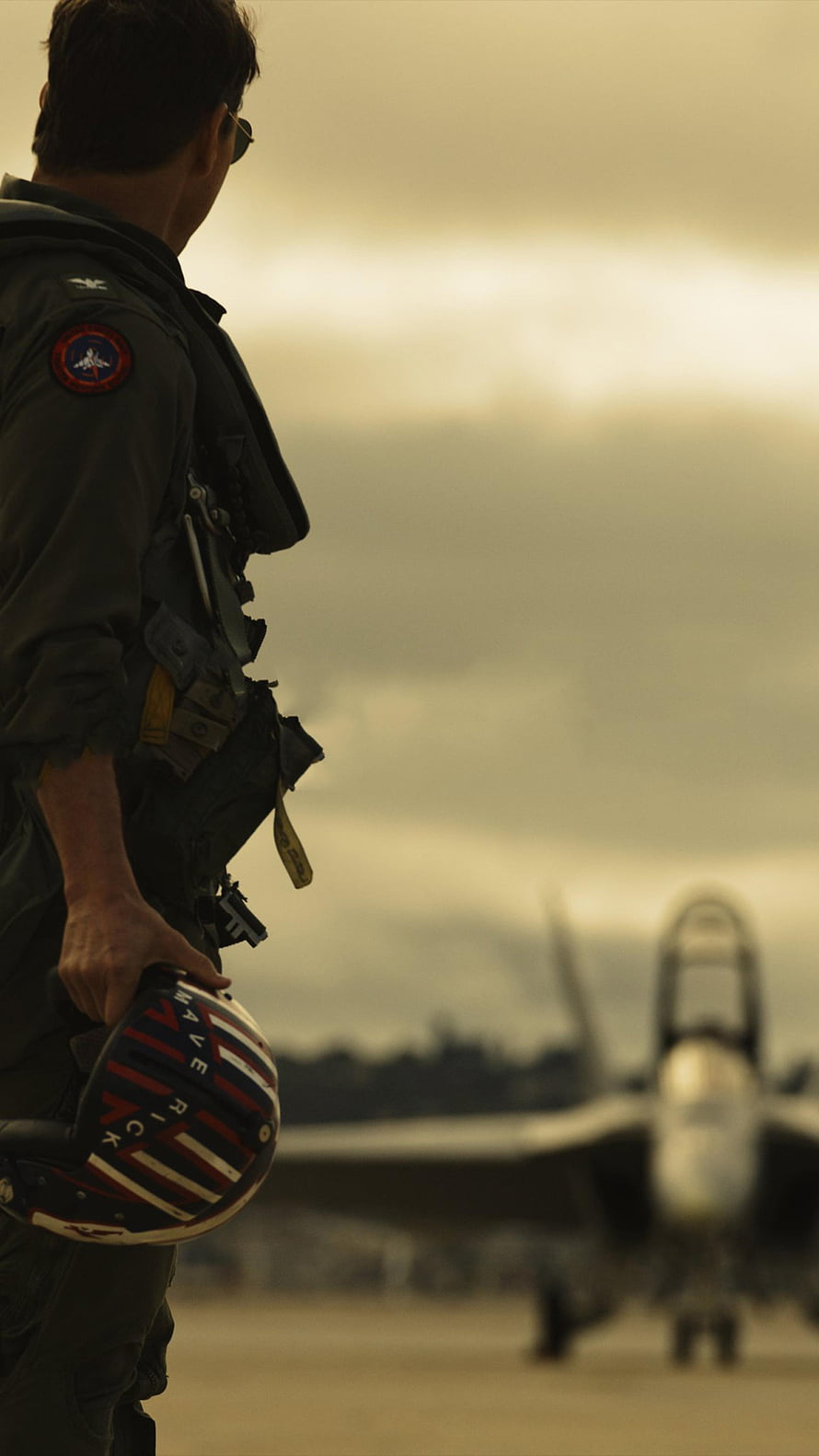 Top Gun Maverick Pilot Holding Helmet on Airfield with Fighter Jet in Background HD phone wallpaper