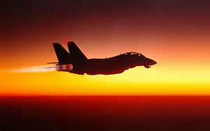 F-14 Tomcat fighter jet silhouette with afterburner against a fiery orange sunset sky HD wallpaper