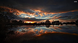Dramatic Sunset Over Calm Lake With Cloud Reflections And Silhouetted Trees HD wallpaper