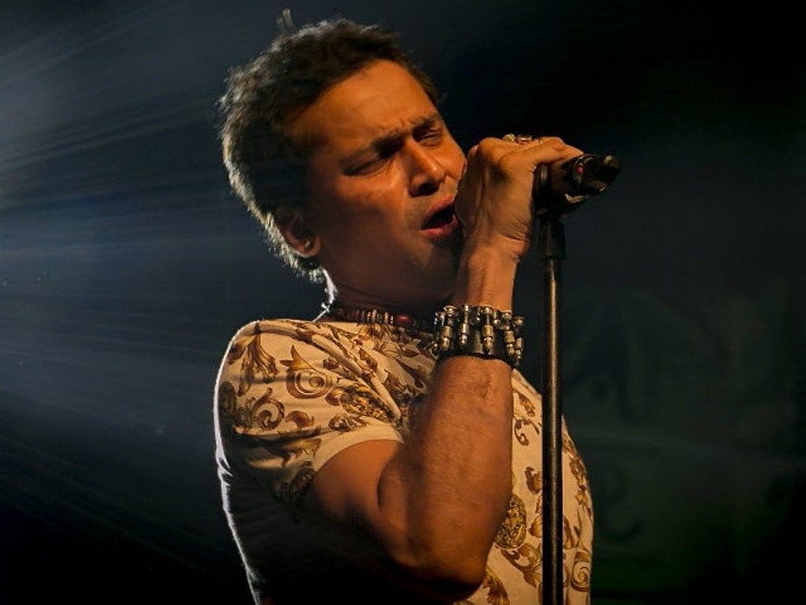 Zubeen Garg performing live on stage with dramatic spotlight and ornate patterned shirt HD wallpaper