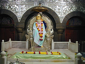 Sai Baba seated on ornate silver throne with floral garlands in temple shrine HD wallpaper