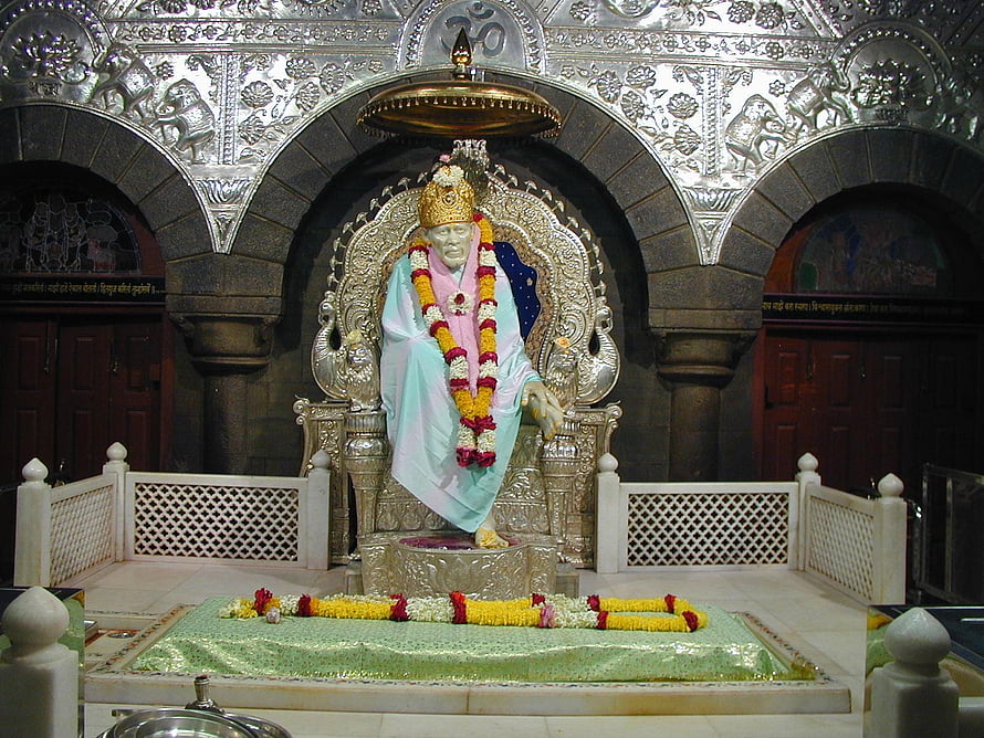 Sai Baba seated on ornate silver throne with floral garlands in temple shrine HD wallpaper