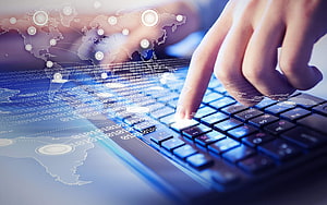 Hands typing on a laptop keyboard with a holographic world map and binary code overlay HD wallpaper