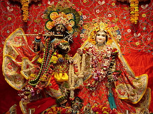 Radha Krishna Deities Adorned in Flowers and Jewels on Red Embroidered Backdrop HD wallpaper