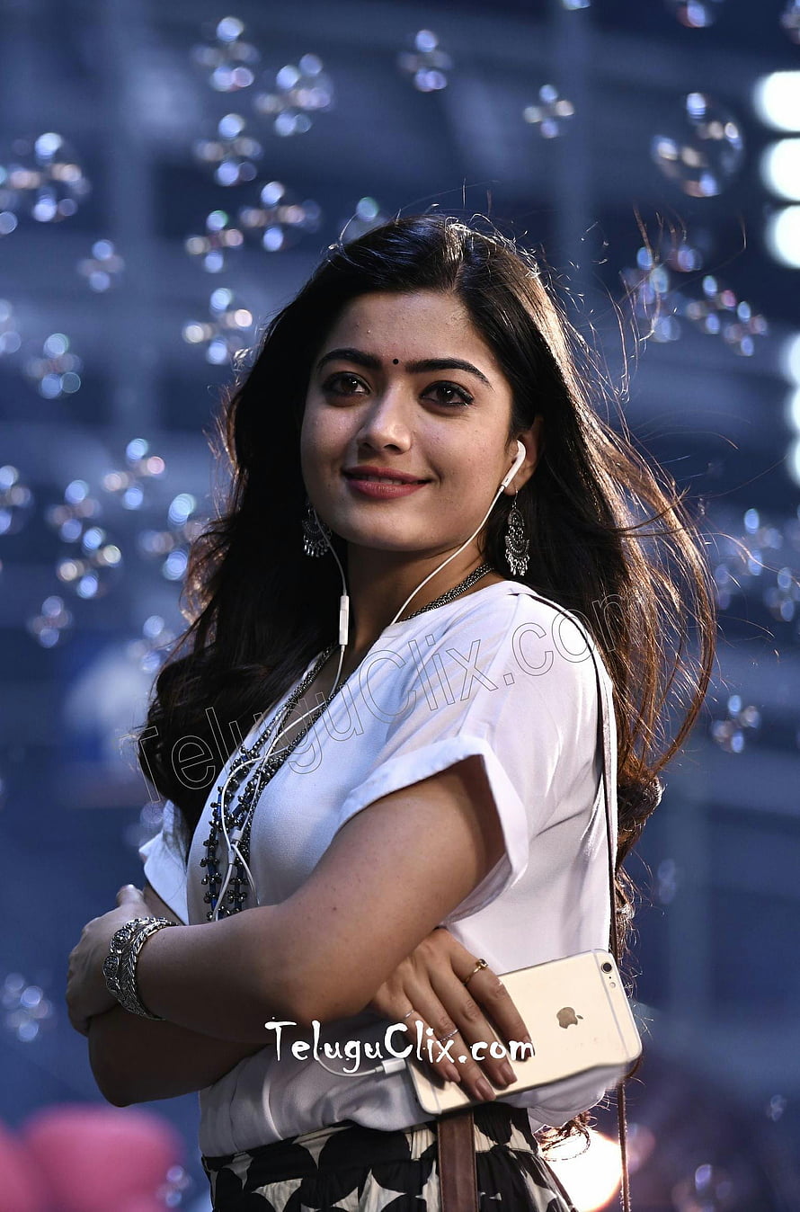 Rashmika Mandanna in White Top with Earphones and Gold Smartphone HD phone wallpaper
