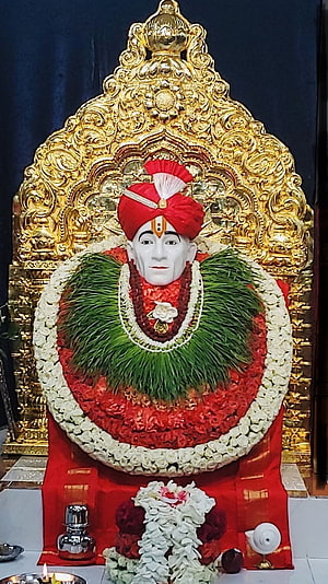 Shri Gajanan Maharaj adorned with floral garlands and a red turban before a golden arch HD phone wallpaper