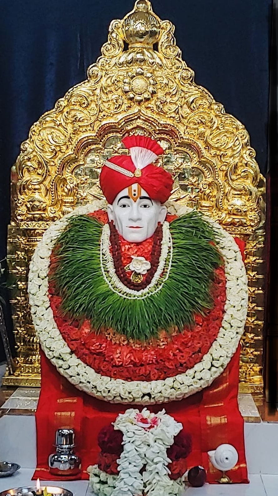 Shri Gajanan Maharaj adorned with floral garlands and a red turban before a golden arch HD phone wallpaper