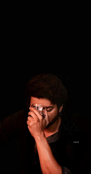 Dhanush in a moody close-up portrait, holding glasses to his face against a dark background HD phone wallpaper