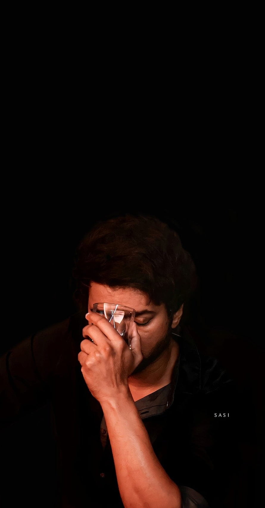 Dhanush in a moody close-up portrait, holding glasses to his face against a dark background HD phone wallpaper