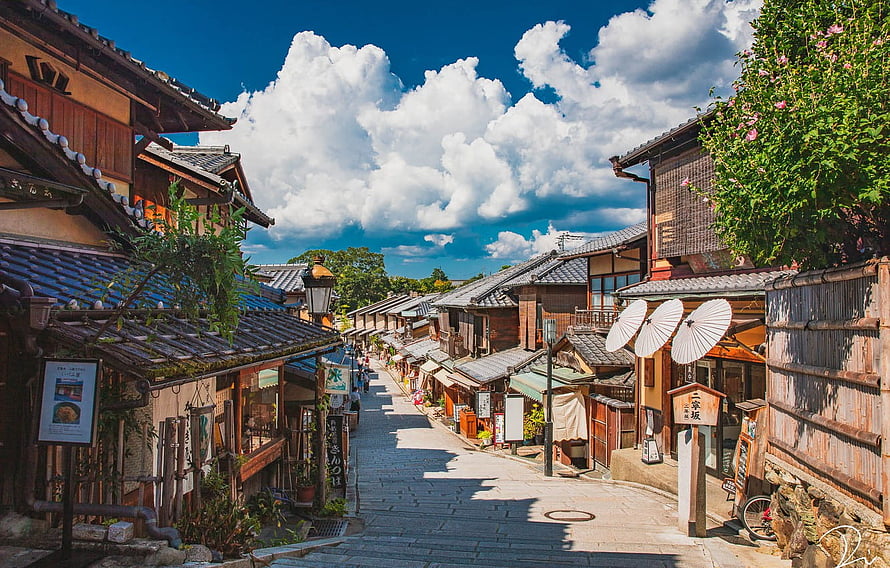 Traditional Kyoto Street Scene With Wooden Houses And Japanese Umbrellas Under A Bright Summer Sky HD wallpaper