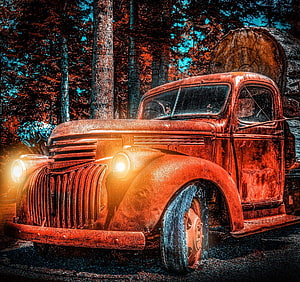 Rusty vintage red pickup truck parked in a forest with glowing headlights and a large log in the background HD wallpaper