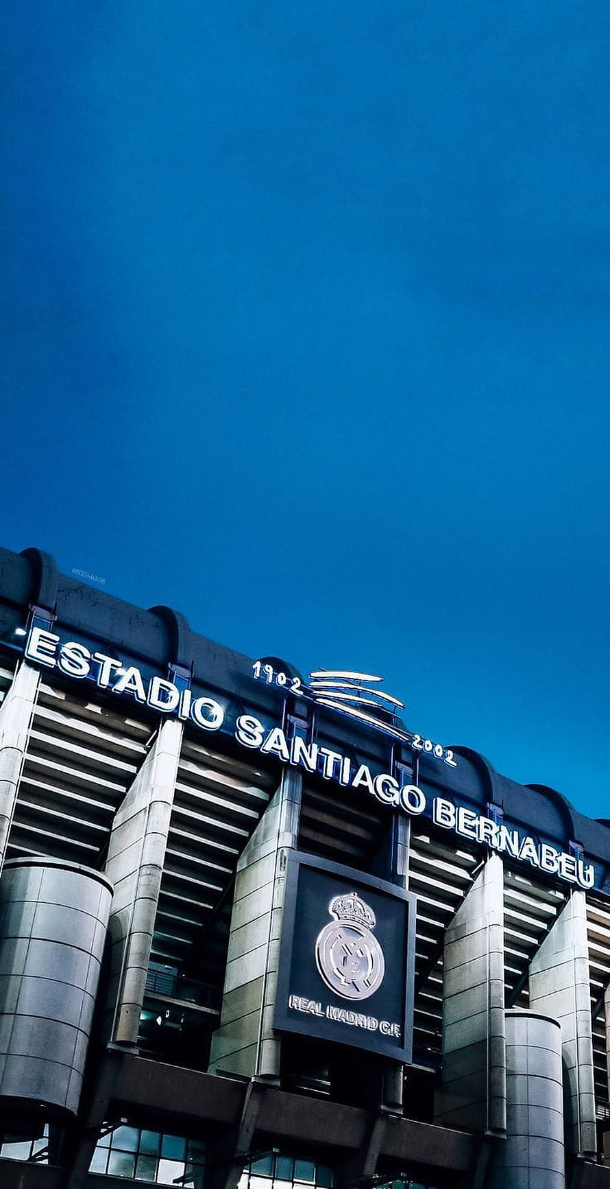 Santiago Bernabeu Stadium Exterior with Real Madrid Crest Against Deep Blue Sky HD phone wallpaper