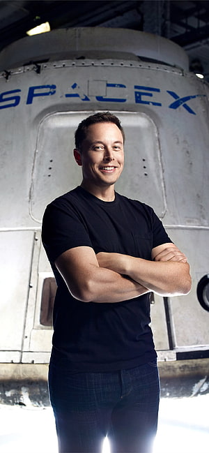 Elon Musk standing with arms crossed in front of a SpaceX rocket capsule HD phone wallpaper
