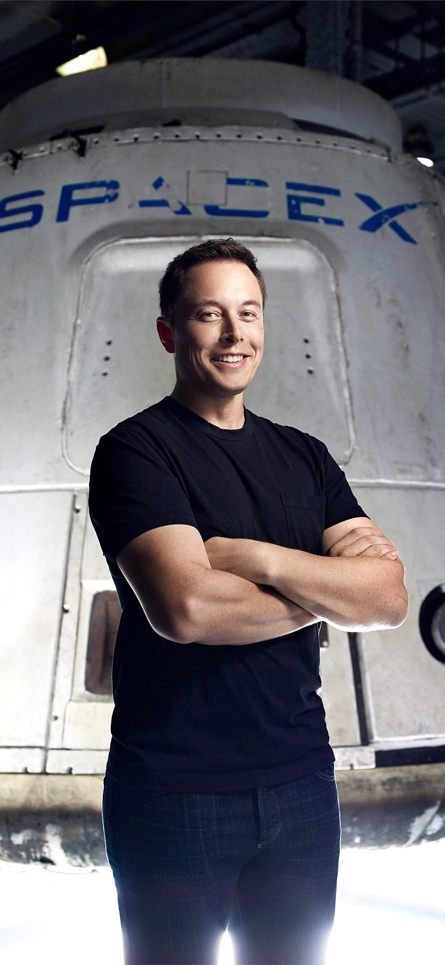 Elon Musk standing with arms crossed in front of a SpaceX rocket capsule HD phone wallpaper