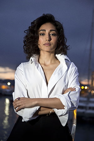 Golshifteh Farahani in a white shirt and black skirt with arms crossed at a waterfront at dusk HD phone wallpaper