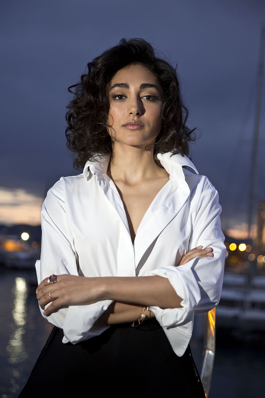 Golshifteh Farahani in a white shirt and black skirt with arms crossed at a waterfront at dusk HD phone wallpaper