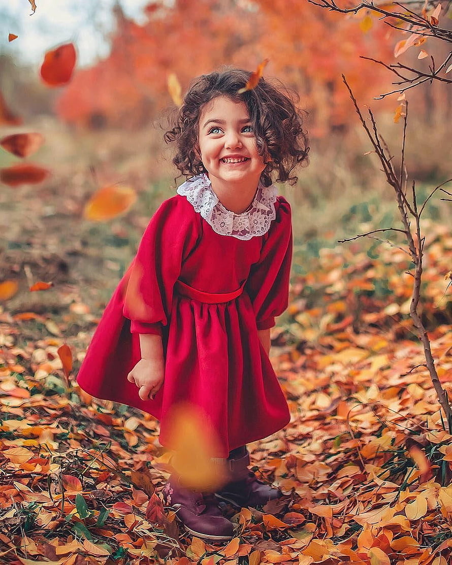 Smiling Curly-Haired Girl in Red Dress Standing in Autumn Leaves HD phone wallpaper