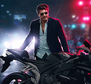 Ajith Kumar in a black suit and sunglasses posing beside a Honda sport motorcycle under neon city lights HD wallpaper