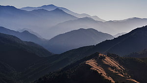 Layered Mountain Ranges in Hazy Blue Mist with Golden Sunlit Ridge HD wallpaper