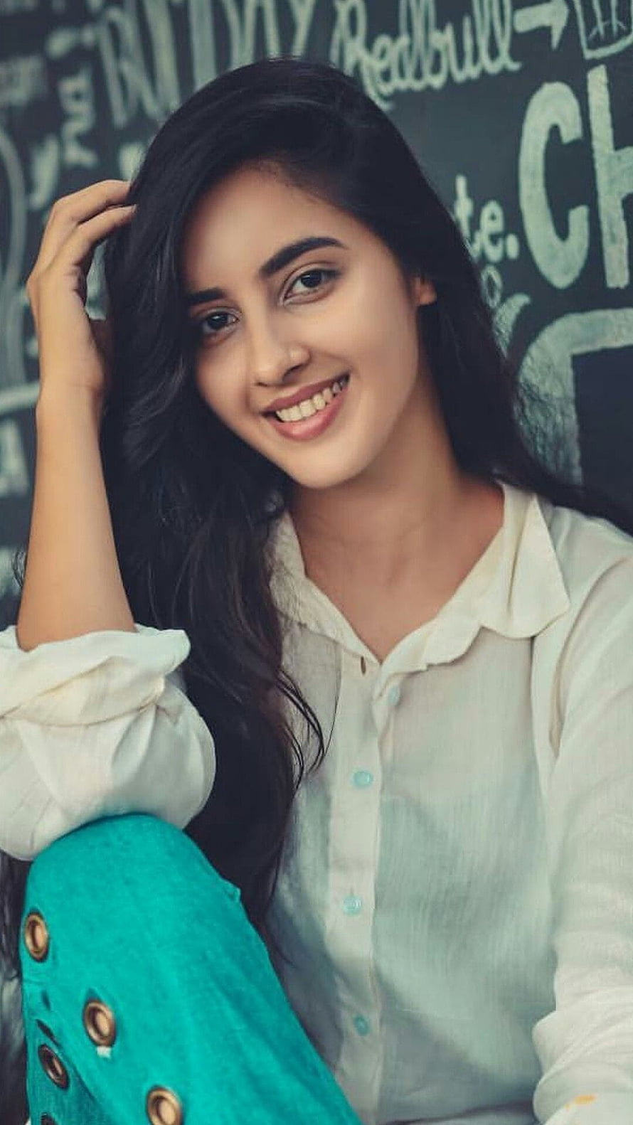 Simrat Kaur smiling portrait in white blouse and teal trousers against a chalkboard background HD phone wallpaper