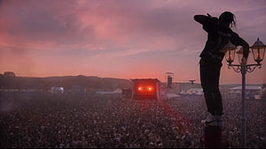 Silhouette of a Performer Standing on a Lamp Post Overlooking a Massive Festival Crowd at Sunset HD wallpaper