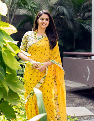 Keerthi Suresh in a Vibrant Yellow Floral Saree Amidst Lush Tropical Greenery HD phone wallpaper