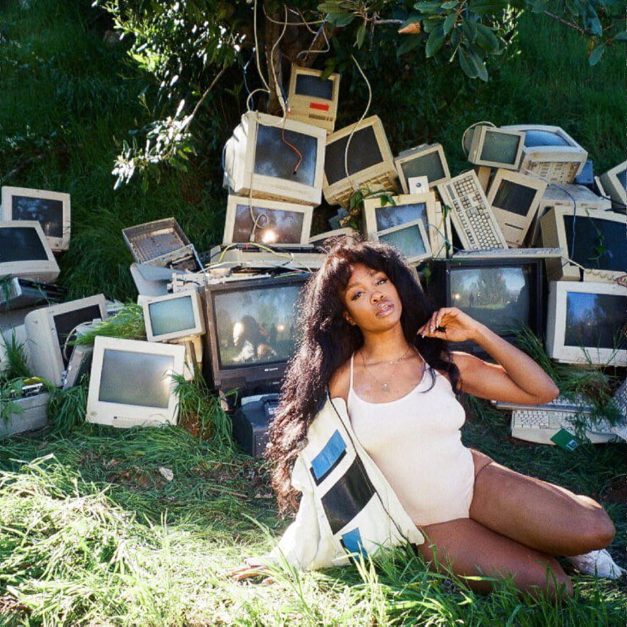 SZA in white bodysuit seated on grass before a pile of vintage CRT monitors and keyboards HD phone wallpaper
