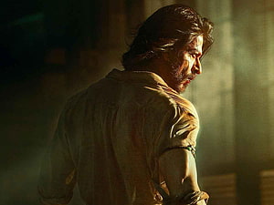 Shah Rukh Khan in intense dramatic profile with bloodied face and torn shirt in dimly lit cinematic scene HD wallpaper