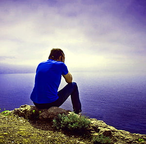Man in blue shirt sitting alone on a rocky cliff overlooking the ocean, Top 125 Feeling Alone Boy Whatsapp dp Pics, feeling boy HD wallpaper