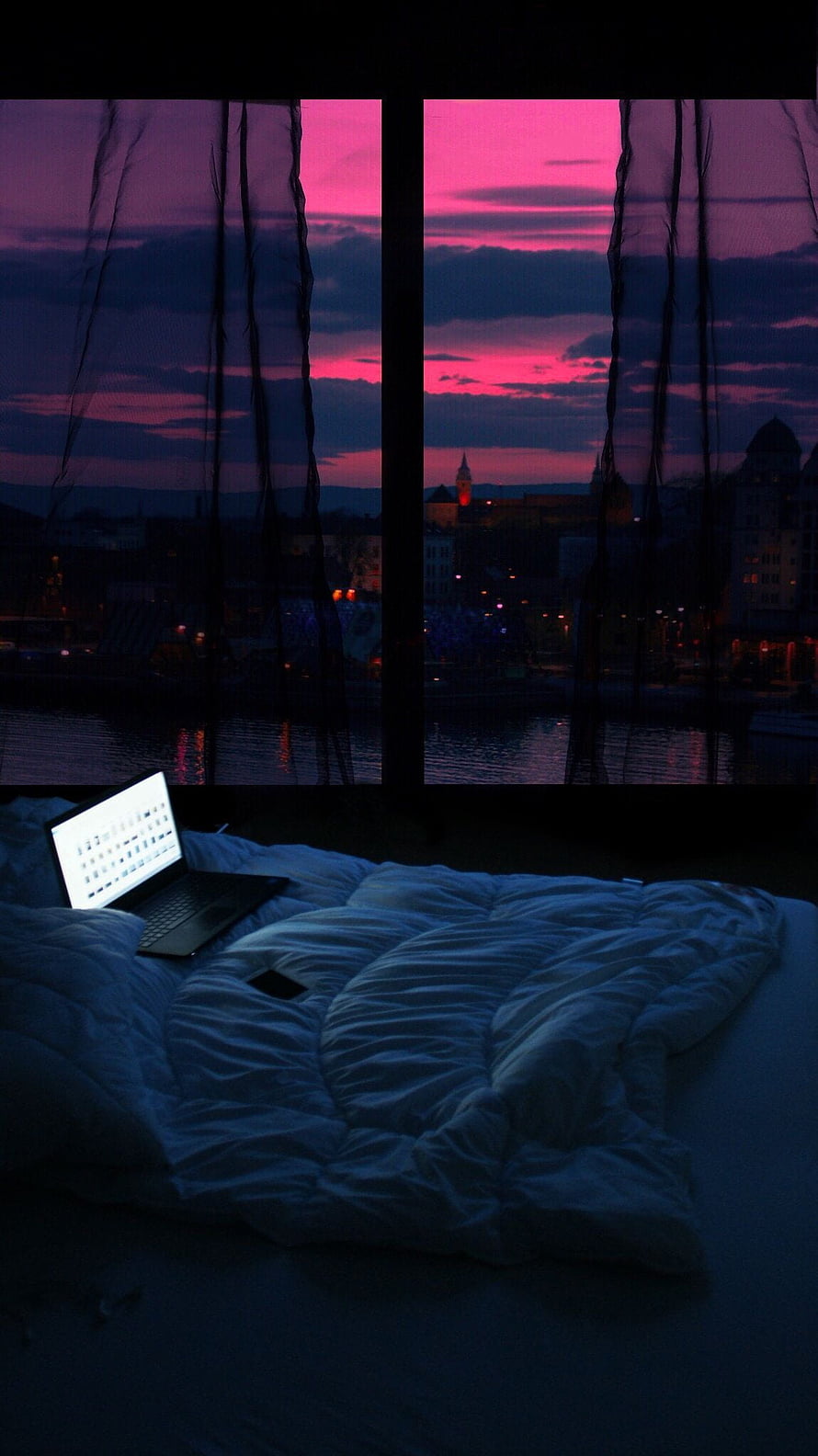 Cozy Bedroom Night Scene with Laptop and Vibrant Pink Sunset City View Through Window HD phone wallpaper