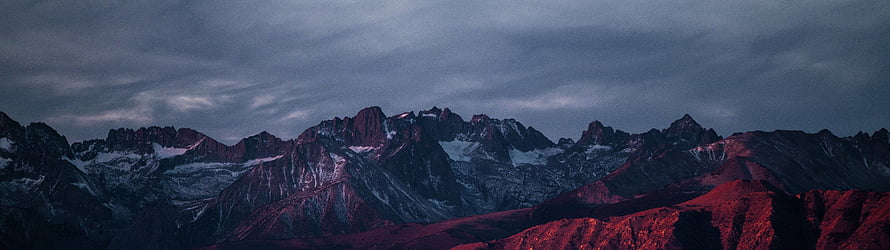 Dramatic Alpine Mountain Range at Dusk with Snow-Capped Peaks and Moody Sky HD wallpaper