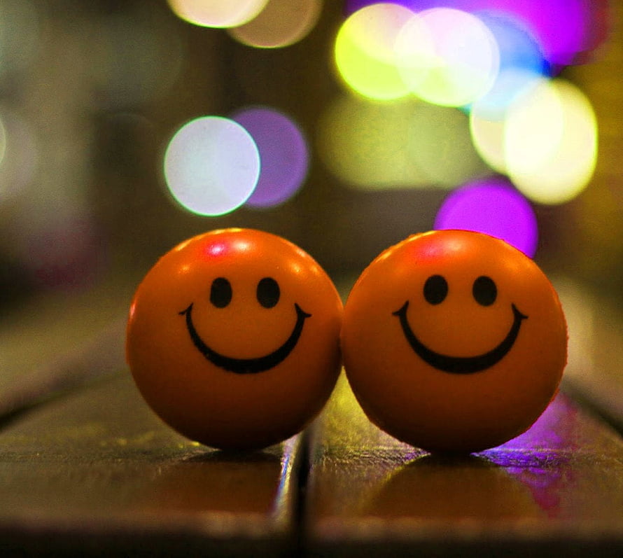 Two Orange Smiley Face Orbs with Colorful Bokeh Lights on a Wooden Surface HD wallpaper