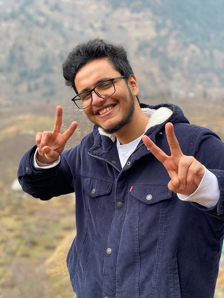 Nischay Malhan Smiling Outdoors in a Navy Jacket with Peace Signs Against a Mountain Backdrop HD phone wallpaper