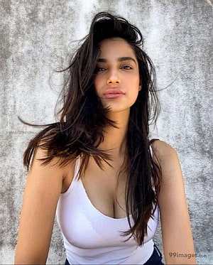Portrait of a woman with long dark hair wearing a white tank top against a textured wall, Meenakshi Chaudhary Latest Hot /, #meenakshi chaudhary HD phone wallpaper