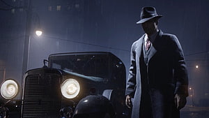 Tommy Angelo in a trench coat and fedora standing beside a vintage car on a rainy night street HD wallpaper