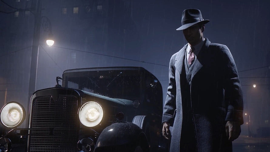 Tommy Angelo in a trench coat and fedora standing beside a vintage car on a rainy night street HD wallpaper
