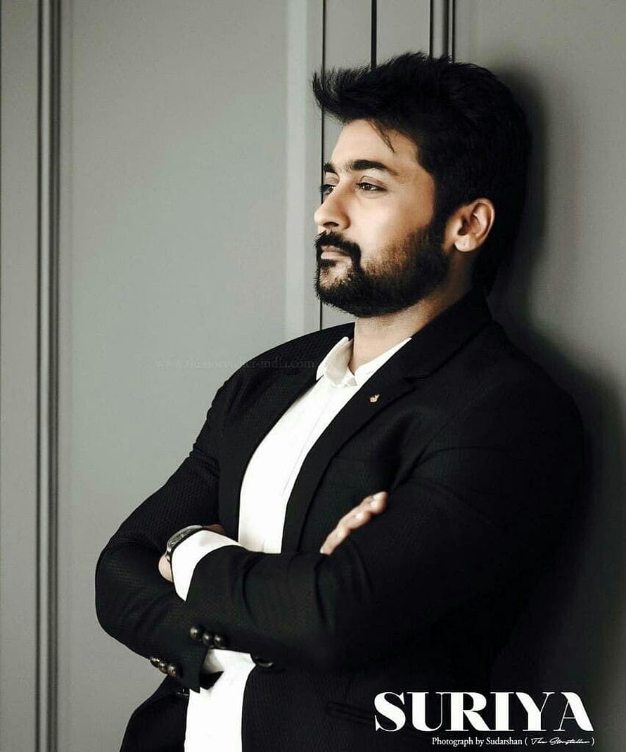 Suriya in a black suit and white shirt leaning against a wall with arms crossed HD phone wallpaper
