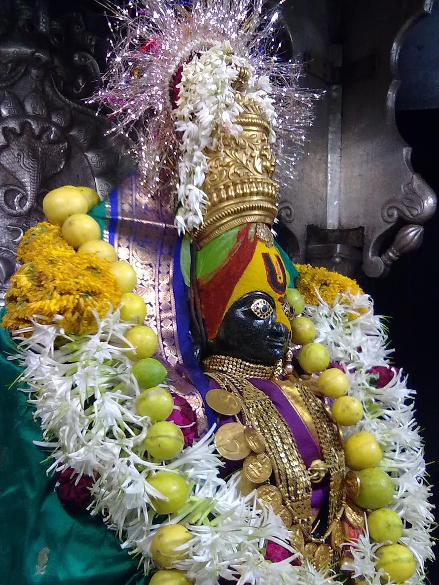 Decorated Hindu deity statue adorned with flowers, fruits, and gold jewelry in a temple setting HD phone wallpaper