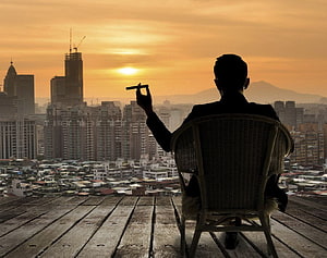 Silhouette of a man in a suit smoking a cigar on a rooftop overlooking a city skyline at sunset, Billionaire Luxury Lifestyle posted by Ryan Walker, billionaire lifestyle HD wallpaper
